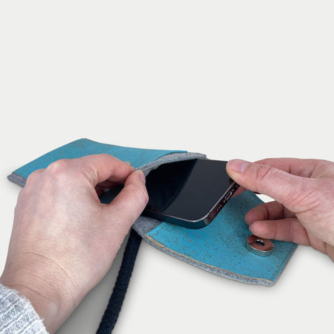 Person, die ein Motorola Razr 60 in eine stilvolle hellgraue und blaue Filztasche mit Schulterriemen steckt.