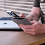 Handytasche für Motorola Edge 50 fusion aus grauem Wollfilz, gehalten von einer Person, mit Laptop im Hintergrund.
